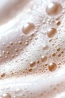 Macro shot of soap bubbles creating abstract pattern with soft beige and white tones, showing delicate surface tension and spherical formations in foam.