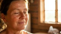Mature woman with closed eyes and peaceful expression in warm sunlight from window, conveying serenity and mindfulness for wellness and lifestyle content.