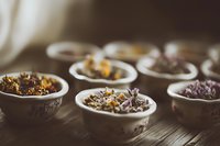 Dried medicinal herbs and flowers in vintage porcelain bowls on rustic wooden table, natural alternative medicine and aromatherapy concept.