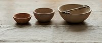 Three handcrafted ceramic bowls in earthy tones arranged on rustic wooden surface with serving utensils for kitchen dining and food preparation.
