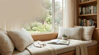 Cozy reading nook with built-in wooden bench, neutral cushions, bookshelf and large window overlooking lush garden for home interior design projects.