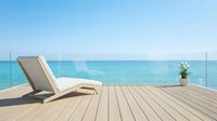 Lounge chair on wooden deck overlooking turquoise ocean and clear sky, ideal for travel, vacation, and resort marketing materials.