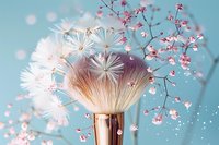 Soft makeup brush with white powder explosion and delicate pink flowers against turquoise background, creating dreamy cosmetic composition for beauty and skincare.