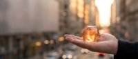 Person holding glowing amber crystal or gemstone in palm against urban street backdrop at golden hour sunset, symbolizing hope, energy, and spiritual wellness for lifestyle and wellness concepts.