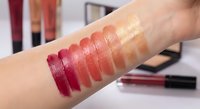 Colorful lipstick swatches on woman's arm showing various shades from deep burgundy to nude pink for cosmetic testing and beauty product selection.
