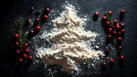 Festive Christmas tree shape made from flour on dark background with fresh cranberries and rosemary sprigs creating holiday baking atmosphere.