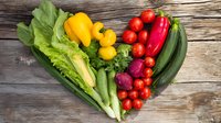 Fresh vegetables arranged in heart shape on rustic wooden background, including lettuce, peppers, tomatoes, and cucumbers for healthy eating concept.