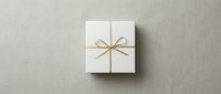 White gift box tied with elegant gold ribbon bow on neutral linen background, top view. Minimalist holiday present for luxury branding.