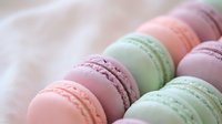 Colorful French macarons in pastel pink and mint green arranged on soft fabric background for bakery menu design and confectionery marketing materials.