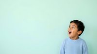 Young boy with dark hair and medium skin tone wearing light blue sweater, looking upward with surprised expression against pale mint green background, suitable for children's education and family lifestyle content.