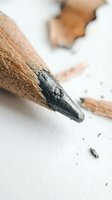 Sharpened graphite pencil tip in close-up with wood shavings and broken lead fragments scattered on white surface, suitable for art, education, and writing concepts.