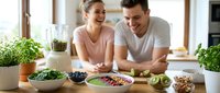 Young couple preparing healthy breakfast together in modern kitchen with fresh fruits, vegetables and smoothie ingredients on wooden table.
