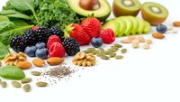 Healthy superfood selection with fresh fruits, vegetables, nuts and seeds arranged on white background for nutritious diet and wellness lifestyle.