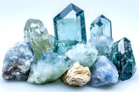Raw aquamarine and blue topaz crystal cluster formation with rough mineral stones on white background, showing natural gemstone structure and color variation.