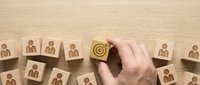 Hand selecting wooden block with target symbol from group of employee icons representing strategic talent acquisition and human resources management.