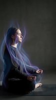 Young woman meditating in lotus position with ethereal blue energy aura flowing around her body creating mystical atmosphere for wellness and spirituality.