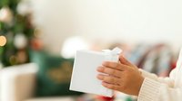 Young woman with medium skin tone holding wrapped white gift box with red ribbon during holiday celebration indoors.