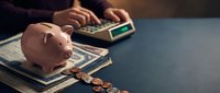 Pink piggy bank on stack of dollar bills with calculator and coins on desk representing personal finance savings and budgeting planning.