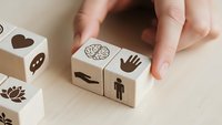 Hand arranging wooden blocks with human icons representing diversity, inclusion and teamwork concepts for business training and development.