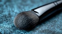 Professional makeup brush with soft bristles on shimmering blue textured surface for cosmetic application and beauty routine enhancement.