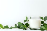 Glass of fresh milk surrounded by green eucalyptus leaves on white background, minimalist composition for dairy products advertising and healthy lifestyle.