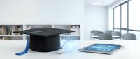Black graduation cap with blue tassel on white desk next to tablet in modern office classroom setting for education achievement and academic success.