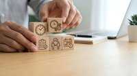 Business professional arranging wooden blocks with time management and productivity icons on office desk for workflow optimization and planning.