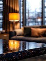 Cozy evening atmosphere with warm lamp light reflecting on glossy black granite countertop, modern living room interior with sofa and window view at dusk.