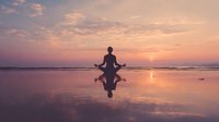 Woman practicing yoga meditation on beach at sunset with perfect reflection in wet sand creating peaceful mindfulness moment for wellness and relaxation.