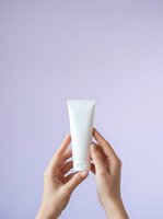 Hands holding white cosmetic tube against lavender background for skincare, beauty, and product packaging mockup applications.