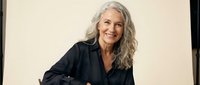 Confident mature Caucasian businesswoman with long gray hair smiling warmly in professional black blazer against neutral background for corporate branding.