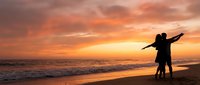 Romantic couple silhouette embracing on beach at sunset with dramatic orange sky and ocean waves, perfect for love and travel concepts.