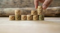Hand placing wooden block with checkmark onto stacked blocks, representing business growth, success, quality assurance, and achievement in corporate environments.