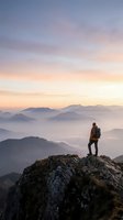 Hiker with backpack standing on rocky mountain peak at sunrise overlooking misty valleys and distant mountains, adventure and exploration concept for travel and outdoor lifestyle.