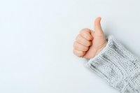 Hand showing thumbs up gesture wearing cozy gray knit sweater sleeve against white background, expressing positivity and approval.