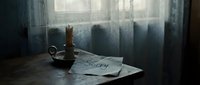 Melancholic scene with a handwritten sorry note and candle on a wooden table near a curtained window in dim light.