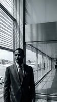 Professional African American businessman in suit standing in modern airport terminal corridor with large windows and contemporary architecture.