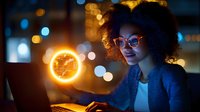 Young African American businesswoman working late at laptop with glowing clock hologram, bokeh lights background, showing work-life balance concept.