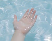 Female hand reaching through crystal clear turquoise water surface creating ripples and reflections, showing tranquility and purity in spa wellness setting.