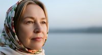 Middle-aged woman with light skin tone wearing a colorful headscarf, gazing toward calm water. Serene portrait for wellness, lifestyle, and contemplation themes.