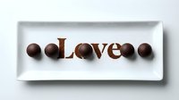 Chocolate truffles and cocoa powder spelling Love on a white rectangular plate, top view, romantic sweet treat concept for Valentine's Day.