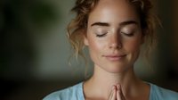 Young Caucasian woman with curly blonde hair in prayer pose, eyes closed in peaceful meditation. Serene expression showing mindfulness and spiritual wellness.