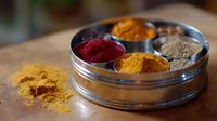 Vibrant colorful spices in round metal container including turmeric, paprika and pepper powder on wooden surface with scattered spice powder. Great for cooking blogs.