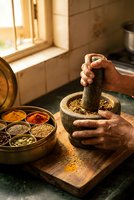 Hands grinding spices in traditional mortar and pestle with colorful spice collection on wooden cutting board in warm sunlit kitchen for cooking preparation.