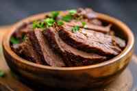 Juicy sliced beef brisket garnished with fresh herbs in wooden bowl, close-up view showing tender meat texture and caramelized edges. For food marketing and menus.