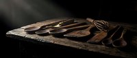 Rustic wooden kitchen utensils and cutting boards arranged on dark wooden table with dramatic lighting for culinary and cooking themes.