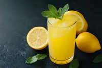 Fresh lemon juice in glass with mint garnish and citrus slices on dark slate background for healthy drinks and summer refreshment concepts.
