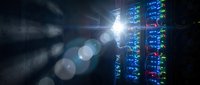 Server racks with glowing blue and red lights in a dark data center, illuminated by bright light rays creating a tech atmosphere.