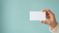 Hand holding blank white business card against soft turquoise background. Ideal for corporate branding, contact information display, and professional marketing materials.