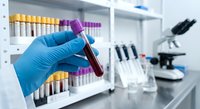 Medical laboratory technician in blue gloves holding blood sample tube with test tubes and microscope in clinical research facility background.